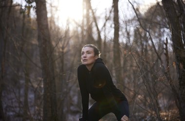 Frau stützt sich mit Hände an Knie im Wald.