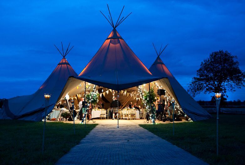 Ein beleuchtetes Tipi-Zelt bei Nacht mit festlicher Dekoration und Gästen im Inneren.