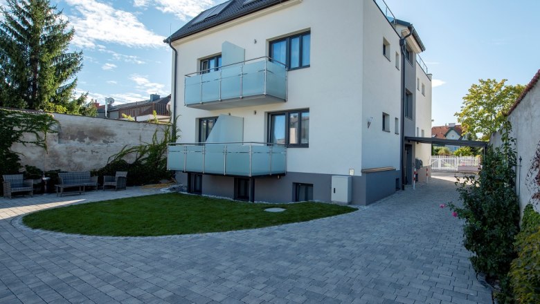 Modernes dreistöckiges Gebäude mit Balkonen und gepflastertem Hof.