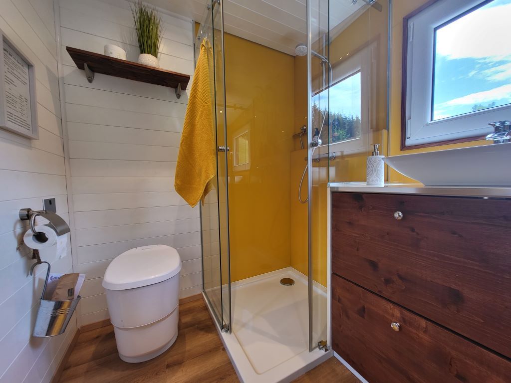 Modernes Badezimmer mit gelber Duschwand, weißem WC, Holzregal und Fenster.
