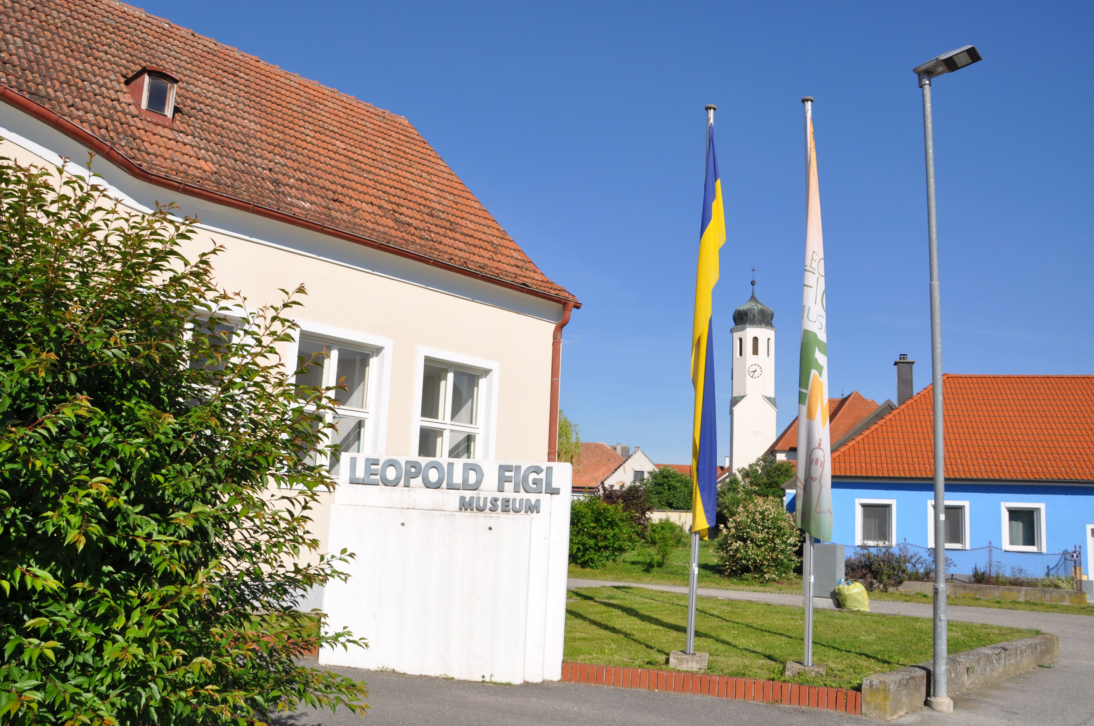 Leopold Figl Museum mit Fahnen und Kirchturm im Hintergrund.