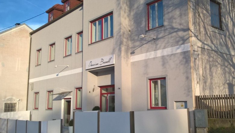 Pension Brandl, © Pension Brandl Außenansicht der Pension Brandl mit grauer Fassade und roten Fensterrahmen.