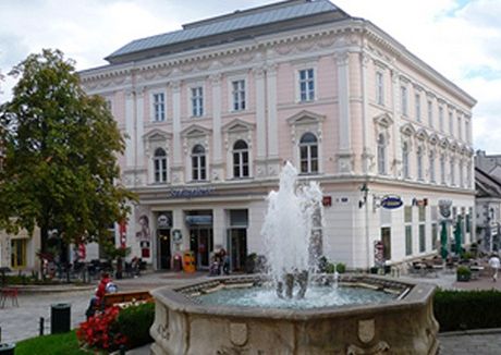 Historisches Gebäude mit Brunnen im Vordergrund.