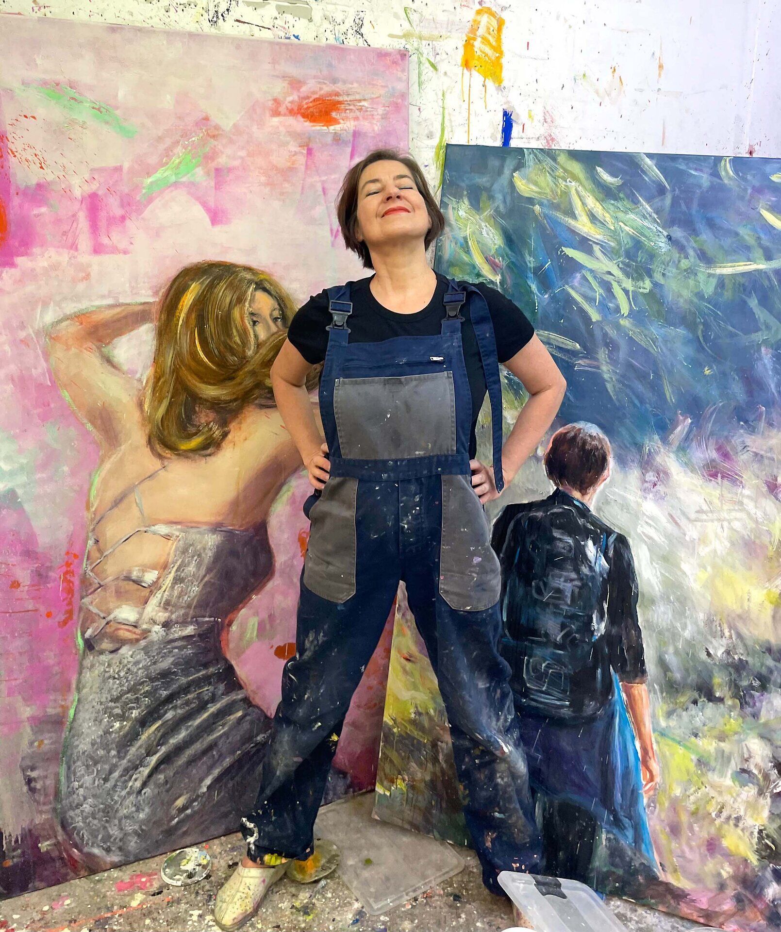 Künstlerin Lisa Kunit steht in ihrem Atelier vor zwei Ölgemälden.