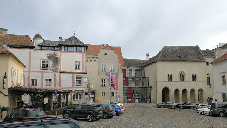Historische Gebäude am Hohen Markt mit geparkten Autos auf Kopfsteinpflaster.