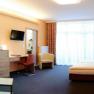 Modern eingerichtetes Hotelzimmer mit Doppelbett, Sofa, Schreibtisch und großem Fenster.