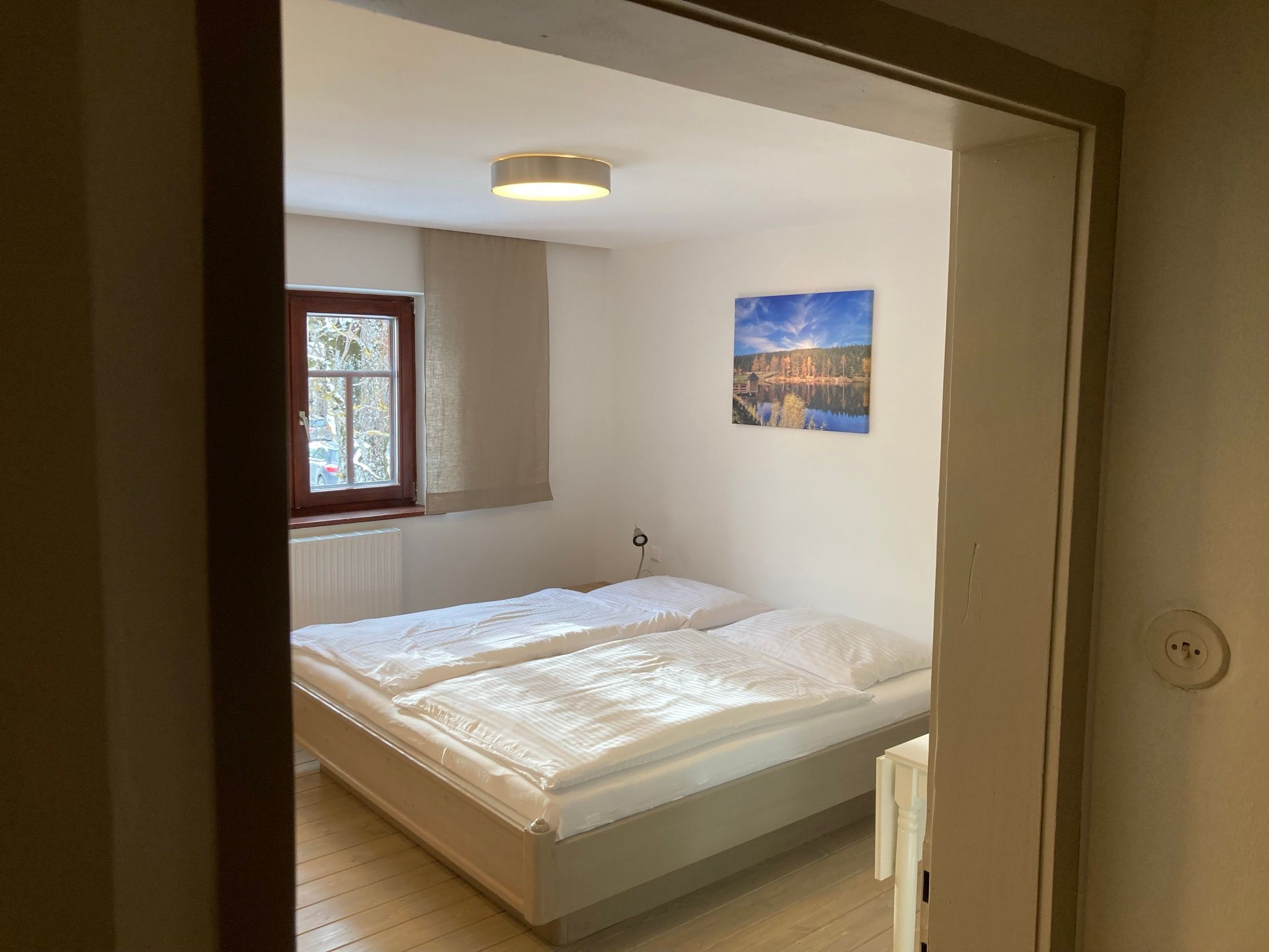 Ein gemütliches Schlafzimmer mit einem Doppelbett, einem Fenster und einem Landschaftsbild an der Wand.