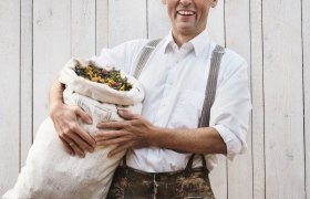 Johannes Gutmann, Gr&uuml;nder von SONNENTOR, h&auml;lt einen Sack voller Kr&auml;uter vor einer Holzwand.