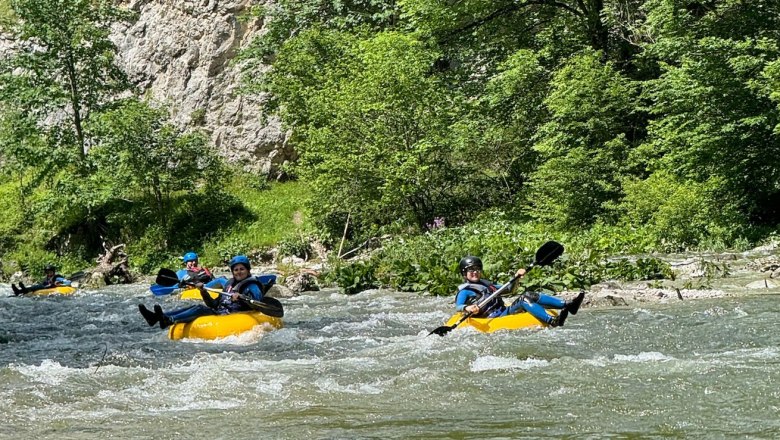 Personen beim Tubing auf einem Fluss in einer grünen, bewaldeten Umgebung.