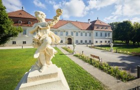 Schloss Marchegg mit Statue im Vordergrund und gepflegtem Garten.