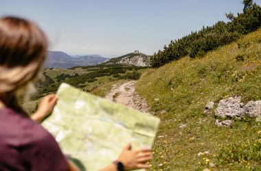 Wanderin mit Wanderkarte blickt auf dem Wanderweg, im Hintergrund Berge &amp; Wiesen