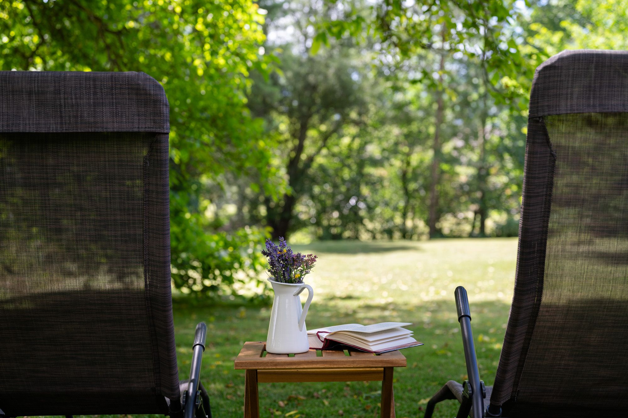 Zwei Liegestühle im Garten mit einem Tisch, auf dem eine Vase mit Blumen und ein Buch stehen.