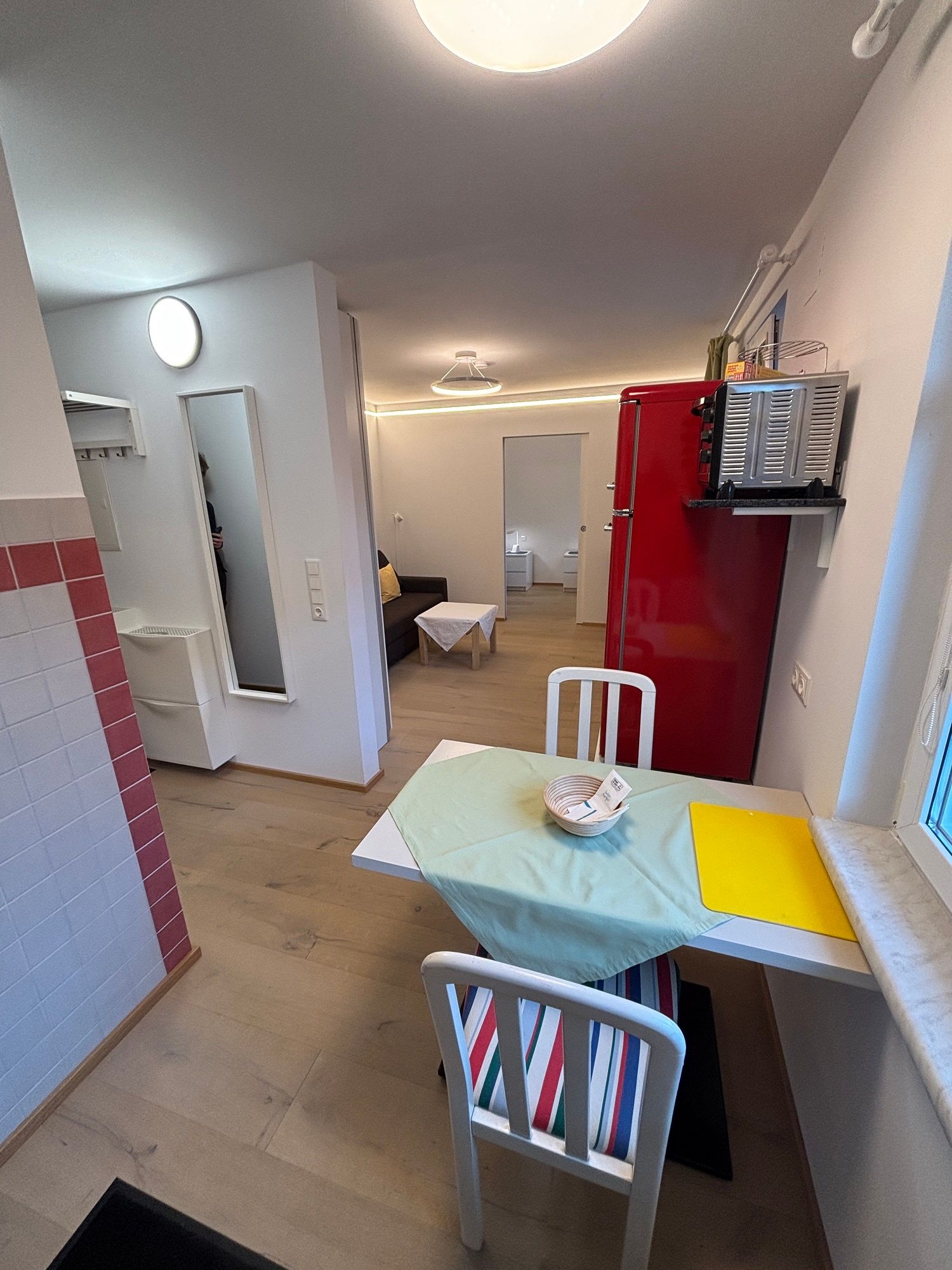 Kleines Wohnzimmer mit Esstisch, Stühlen, rotem Kühlschrank und Sofa.