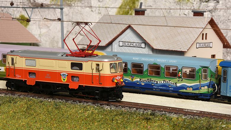 Modelleisenbahn mit Lokomotive und Waggon vor einem Miniaturbahnhof.