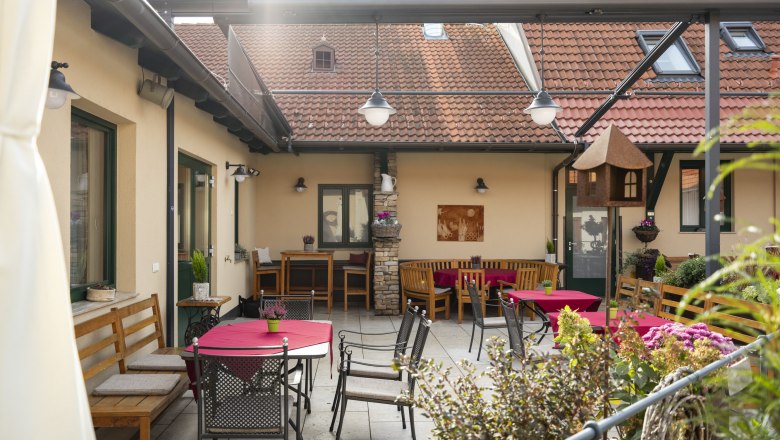 Gem&uuml;tlicher Innenhof mit Sitzgelegenheiten und roten Tischdecken.