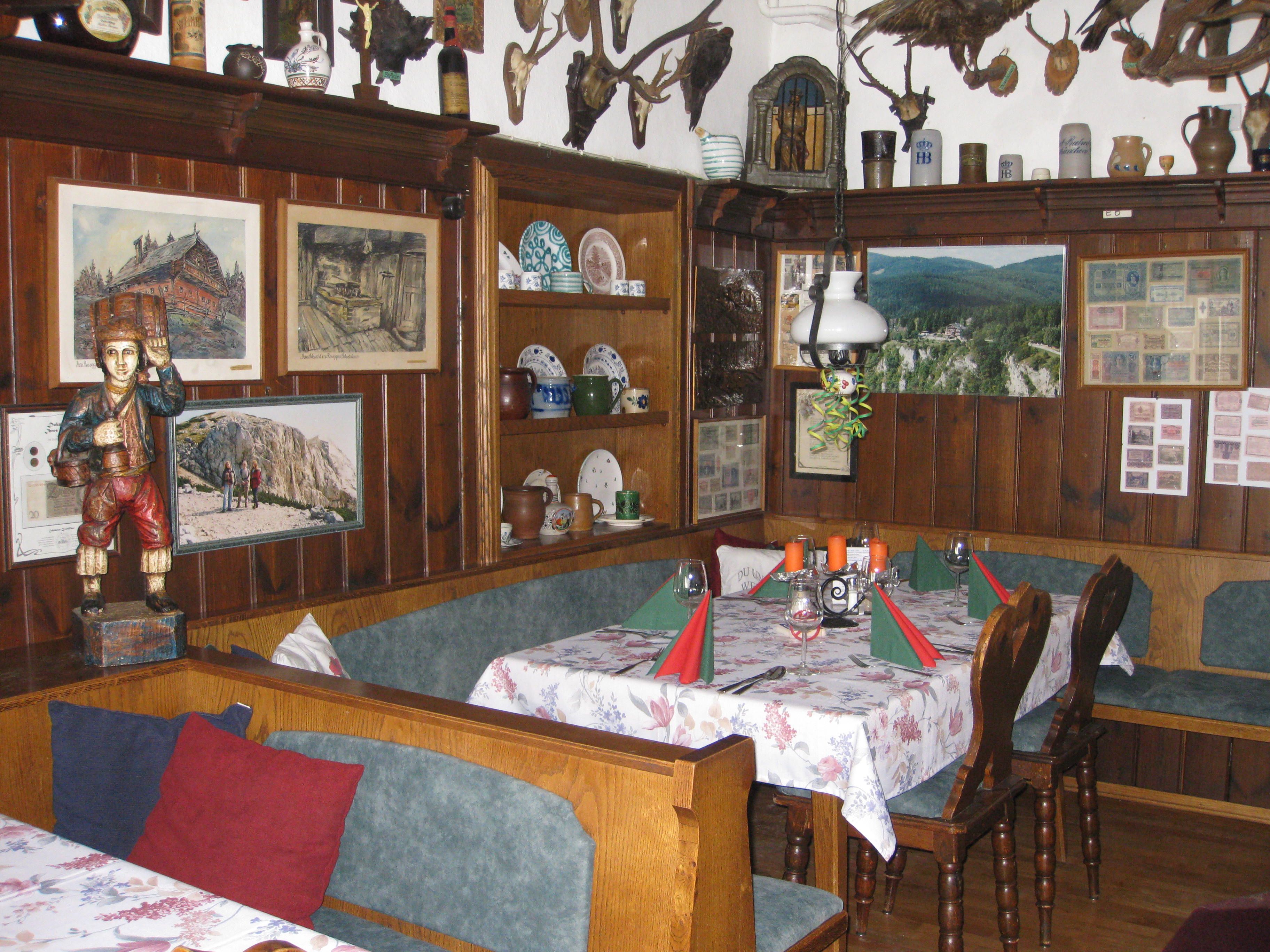 Rustikale Gaststube mit Holzmöbeln, Wanddekorationen und gedecktem Tisch.