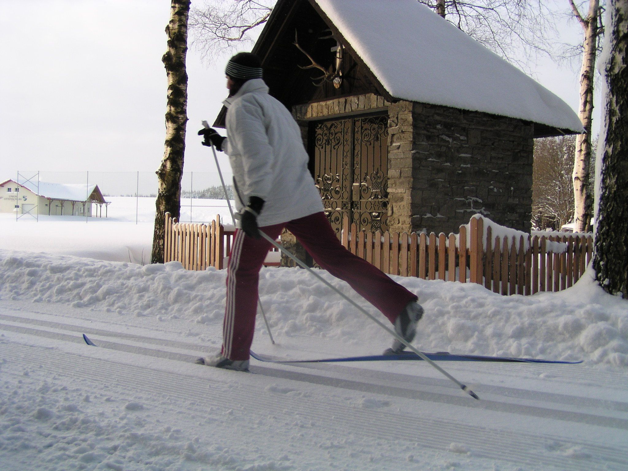 Person beim Langlaufen vor einer verschneiten Kapelle.