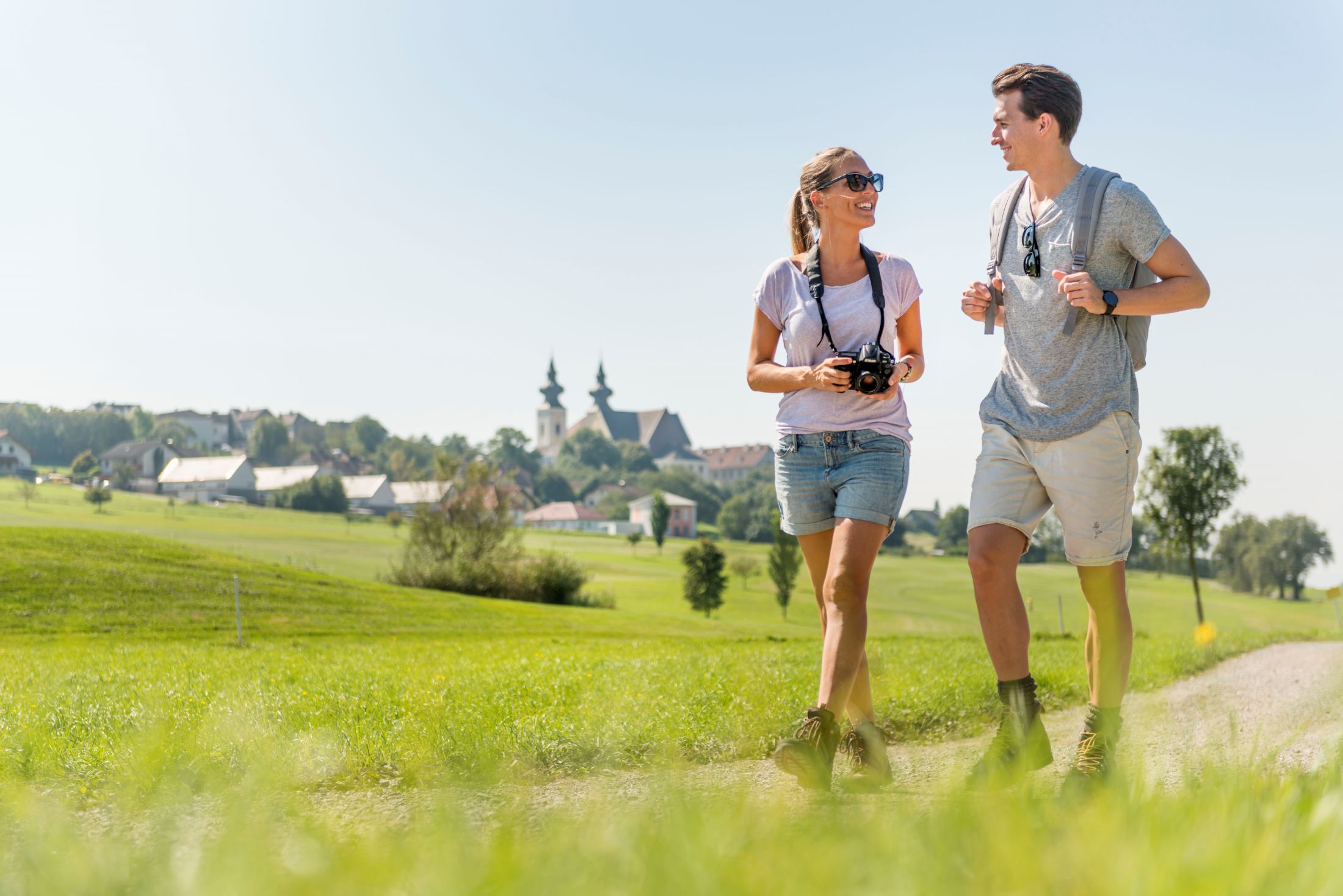 Ein Paar wandert auf einem Feldweg mit einer Kirche im Hintergrund.