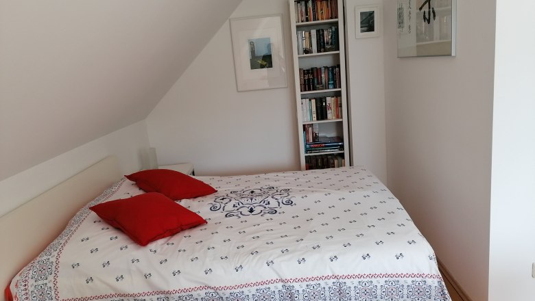 Schlafzimmer mit Bett, roten Kissen und Bücherregal.