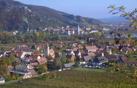 Panorama einer malerischen Stadt mit Weinbergen und einem Fluss im Hintergrund.