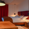 Gemütliches Hotelzimmer mit Doppelbett, rotem Vorhang und Holzmöbeln.