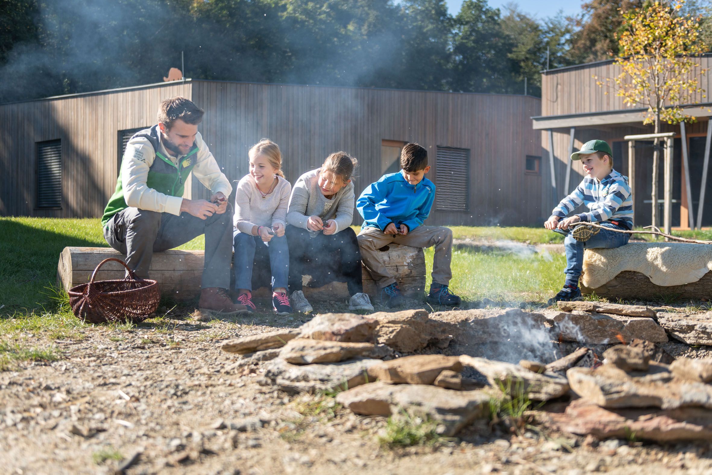 Gruppe von Kindern und einem Erwachsenen am Lagerfeuer im Freien.
