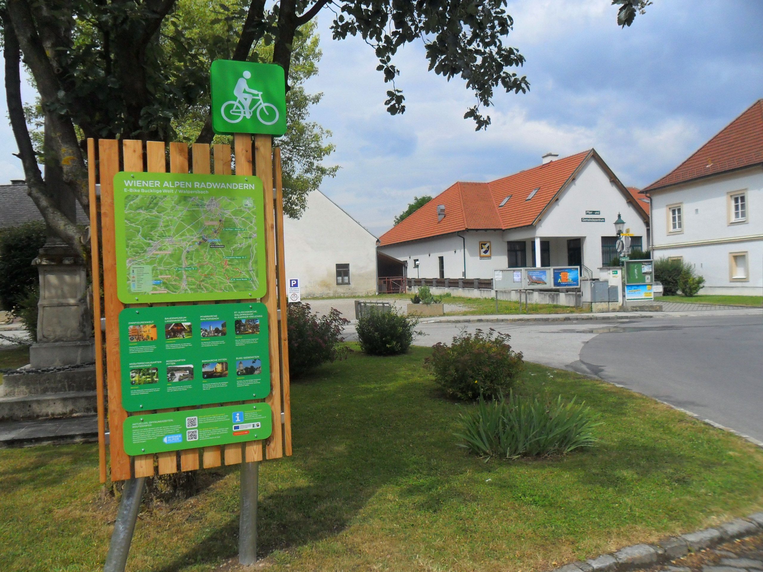 Radstartplatz-Tafel in Walpersbach mit Karte und Informationen, umgeben von Gebäuden und Bäumen.