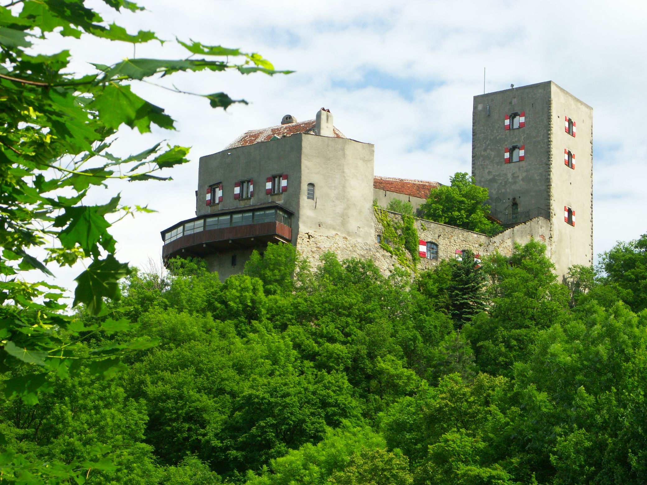 Burg Greifenstein auf einem bewaldeten Hügel mit blauem Himmel im Hintergrund.