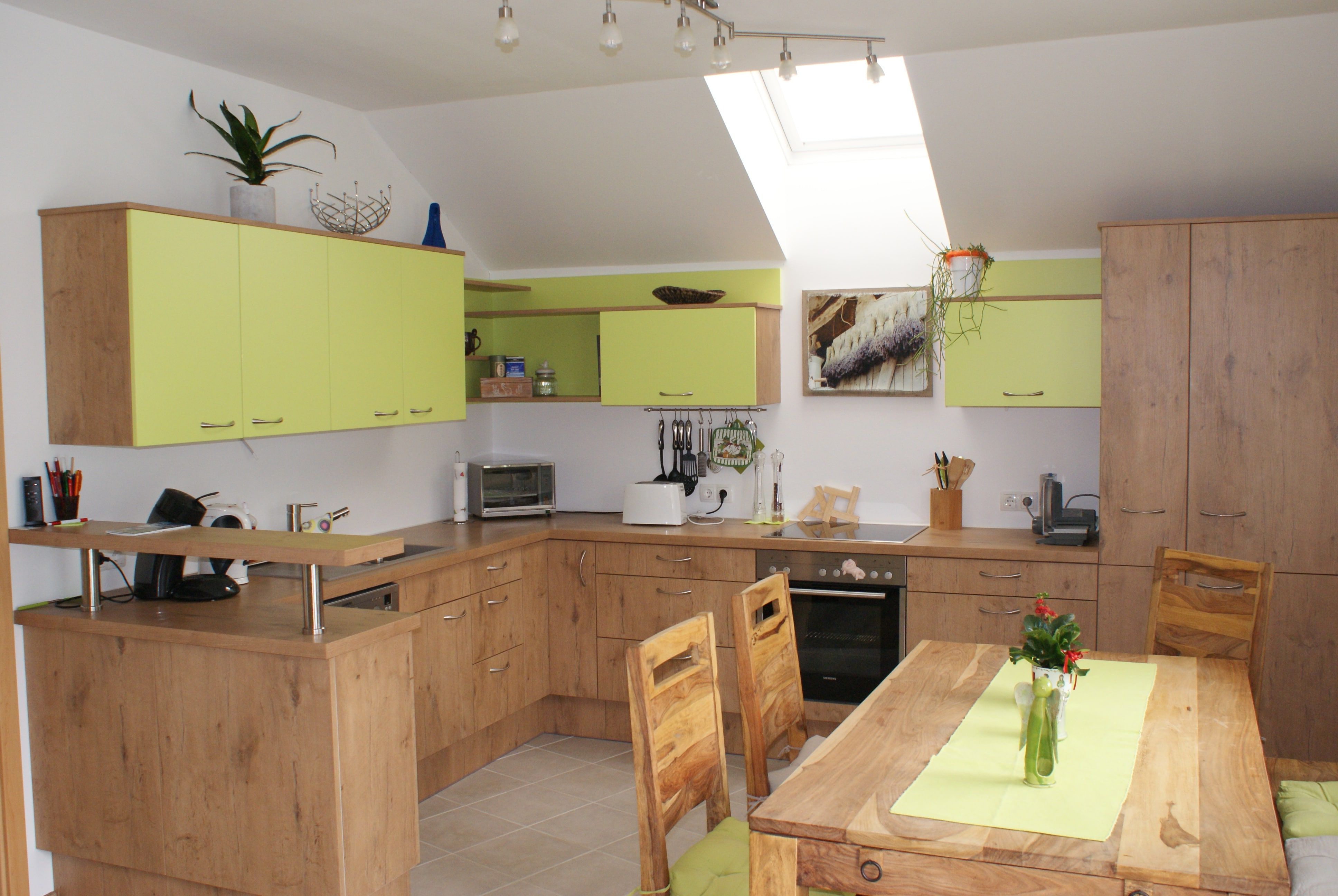 Moderne Küche mit Holzmöbeln und grünen Akzenten, Esstisch mit Vase, Oberlichter.