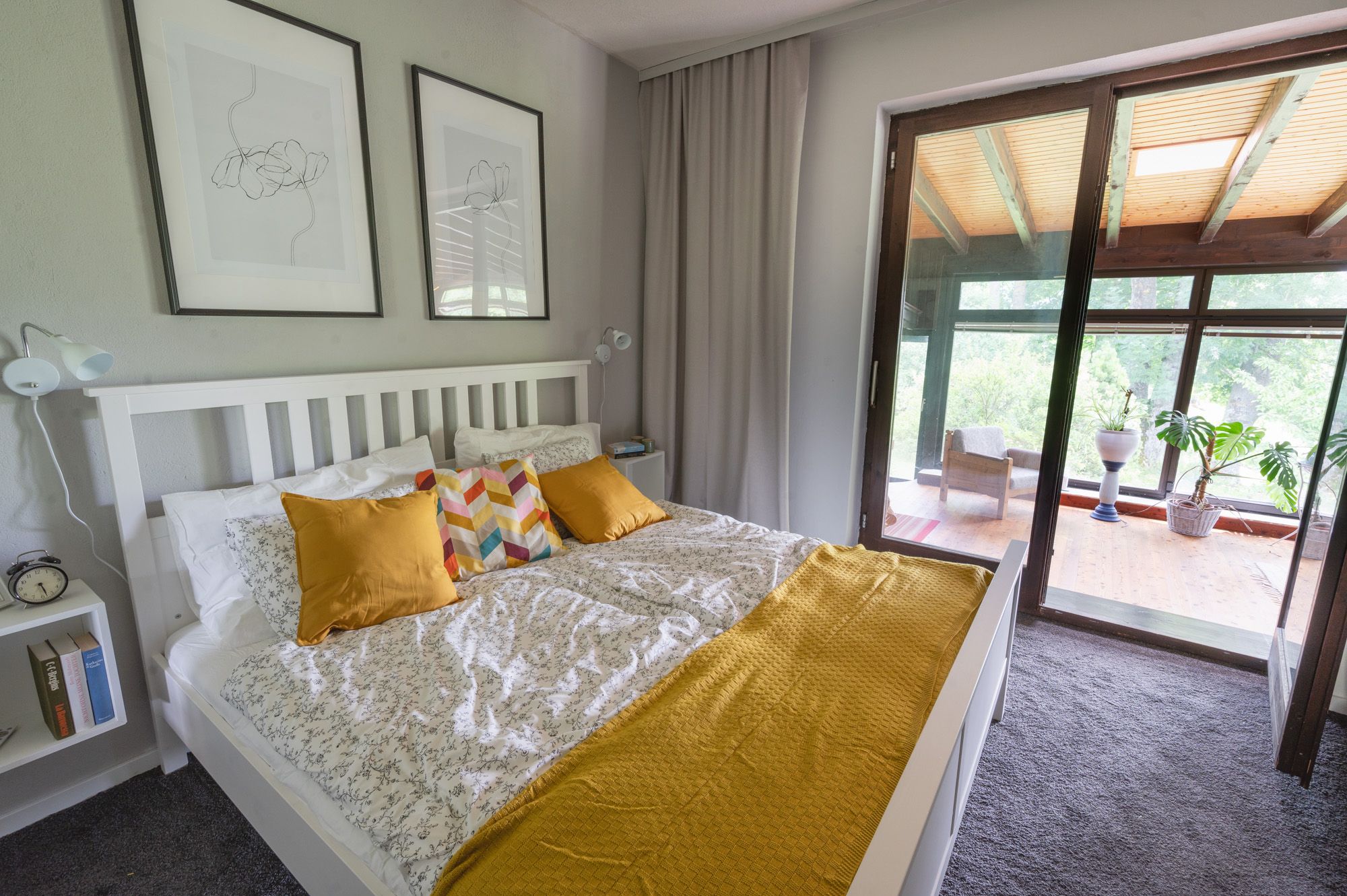 Ein gemütliches Schlafzimmer mit einem weißen Bett, gelben Kissen und einer Terrasse mit Pflanzen im Hintergrund.