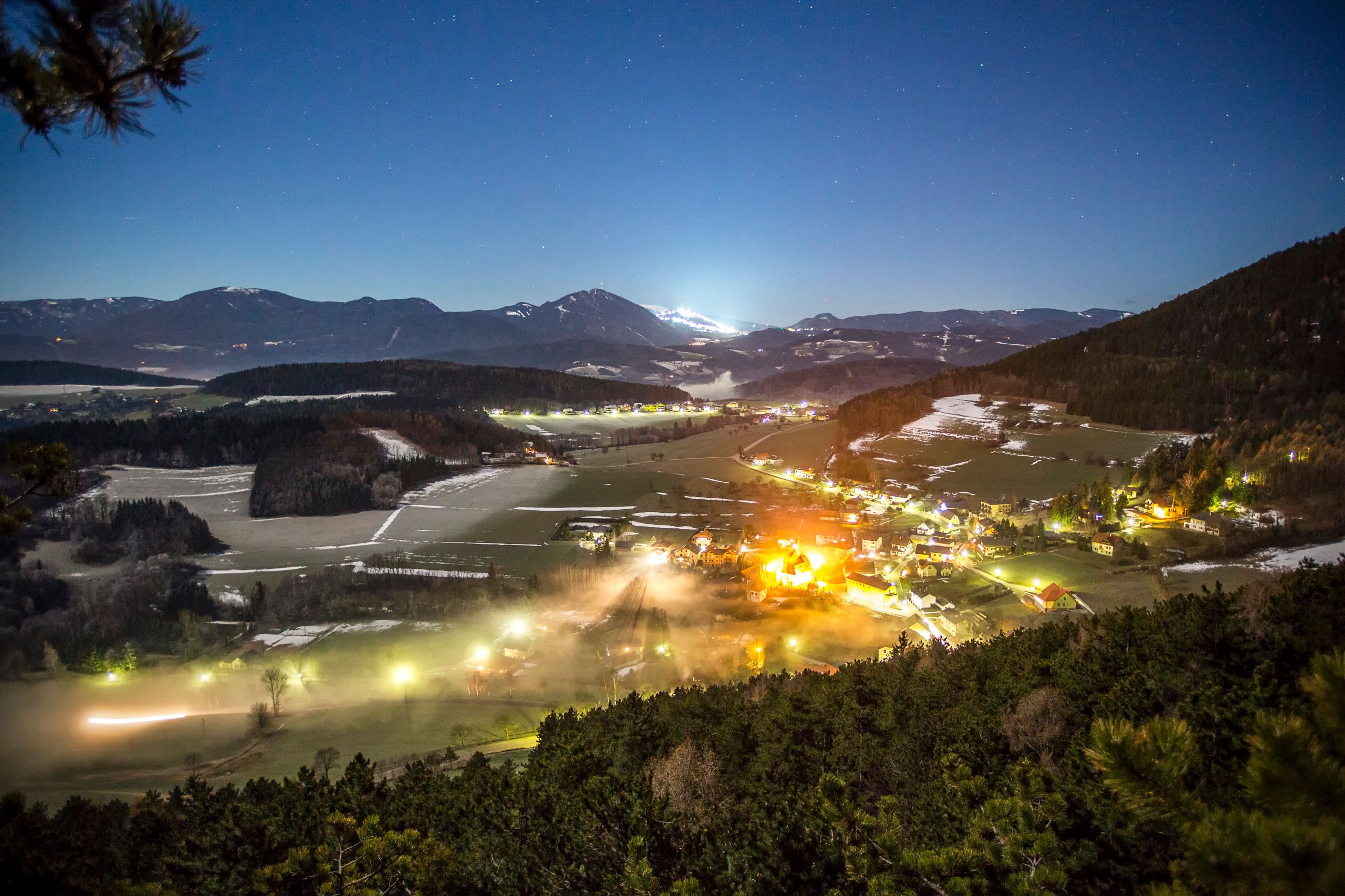 Nächtliche Landschaftsansicht von Prigglitz mit beleuchteten Häusern und Bergen im Hintergrund.