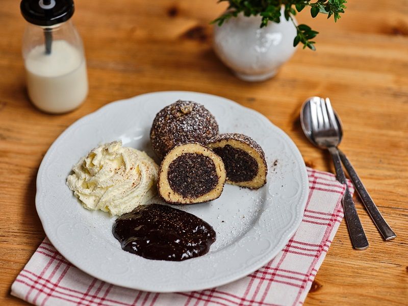 Teller mit Mohnknödeln, Sahne und Schokoladensauce auf Holztisch.