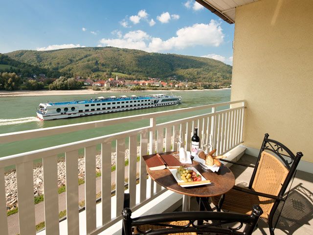 Balkon mit Tisch, Wein und Snacks, Blick auf Fluss und vorbeifahrendes Schiff.
