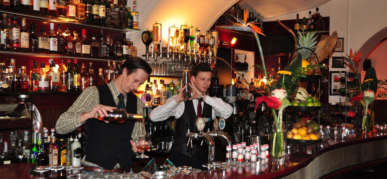 Zwei Barkeeper arbeiten in einer stilvollen Bar mit vielen Flaschen im Hintergrund.