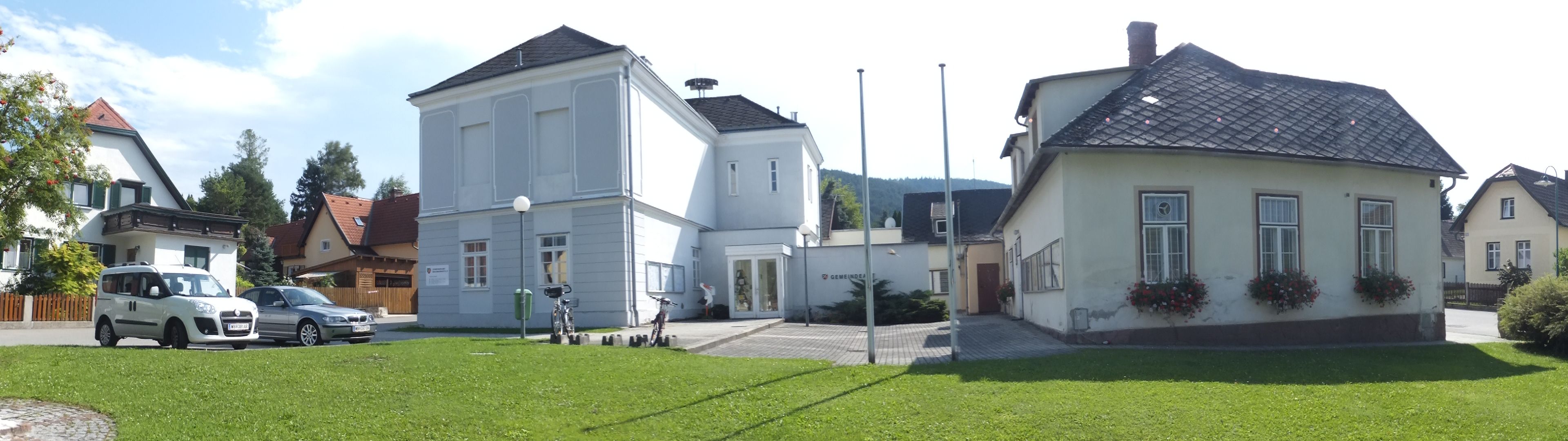 Panoramabild des Gemeindeamts Waidmannsfeld mit umliegenden Gebäuden und Autos.