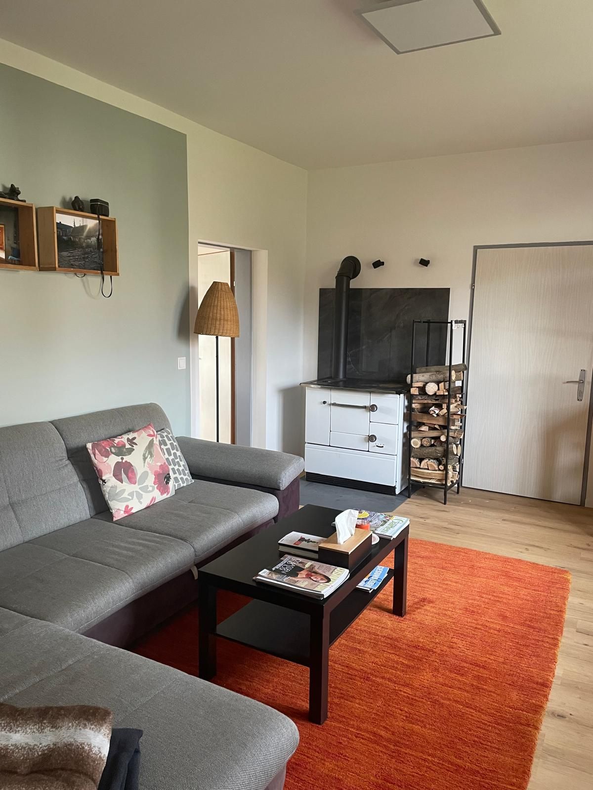 Gemütliches Wohnzimmer mit grauem Sofa, Couchtisch, rotem Teppich und Holzofen.