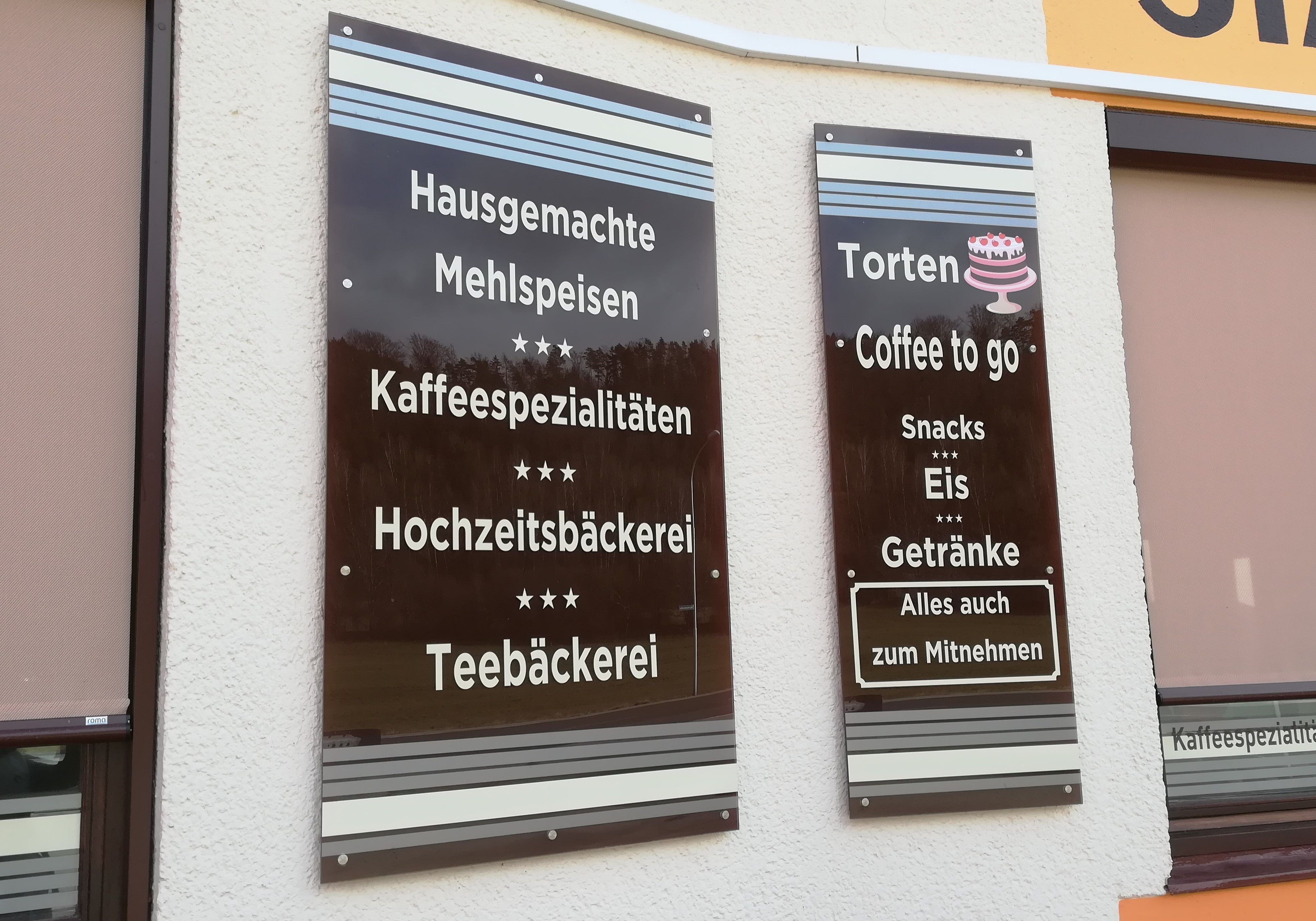 Zwei braune Schilder an der Wand mit Angeboten eines Kaffeehauses wie Mehlspeisen und Eis.