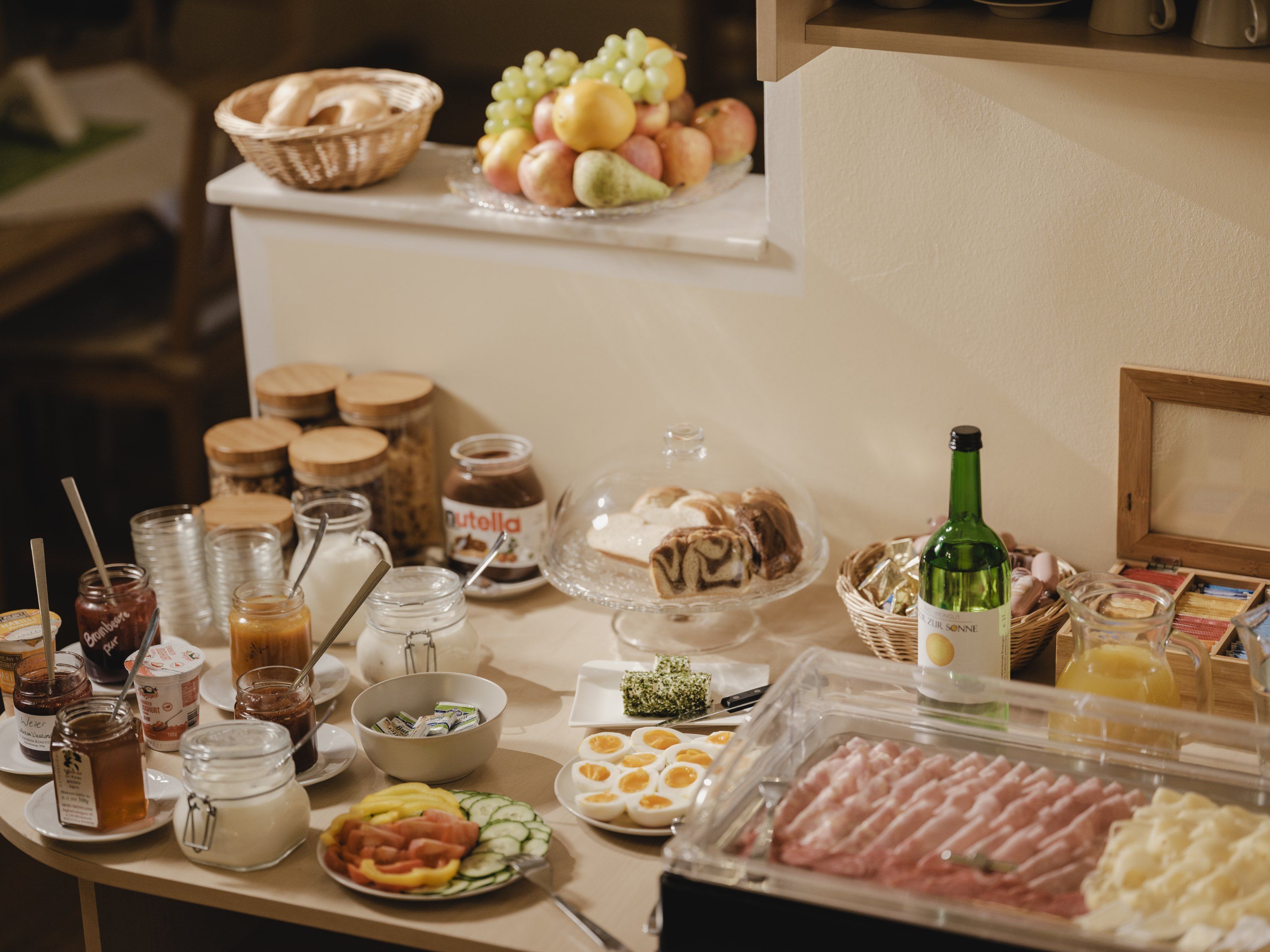 Frühstücksbuffet mit Brot, Aufschnitt, Obst und Getränken.