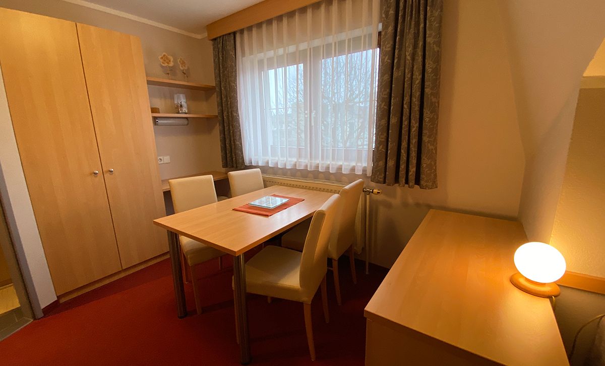 Ein gemütlicher Raum mit Holzmöbeln, Tisch, Stühlen und einem Fenster mit Vorhängen.