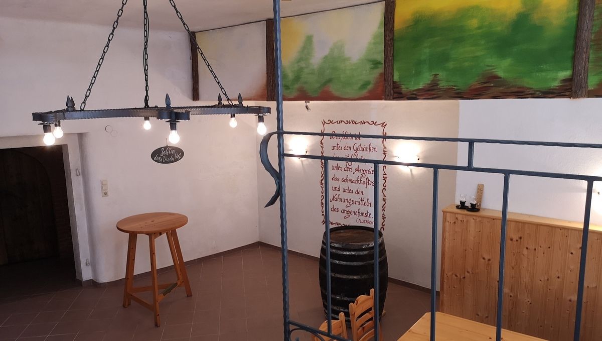 Innenansicht eines rustikalen Kellers mit Holztisch, Weinfass und Wanddekoration.