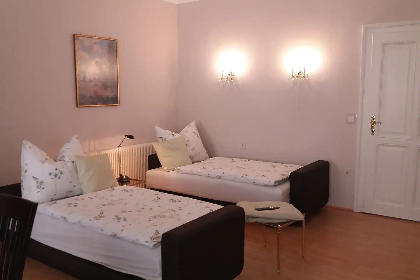 Zwei Einzelbetten in einem hellen Raum mit Wandlampen und einem Gemälde an der Wand.