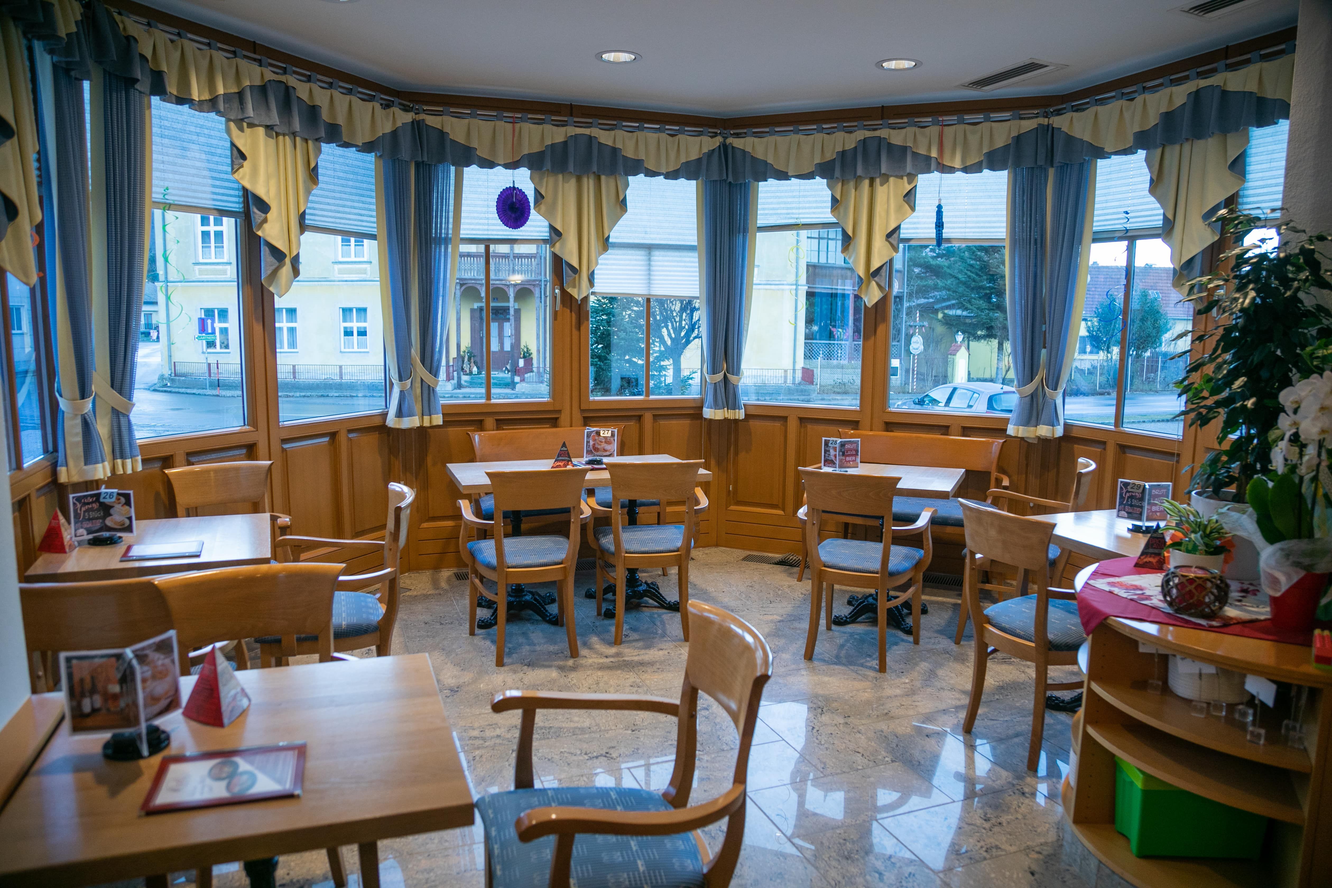 Innenansicht eines gemütlichen Cafés mit Holzmöbeln und großen Fenstern.