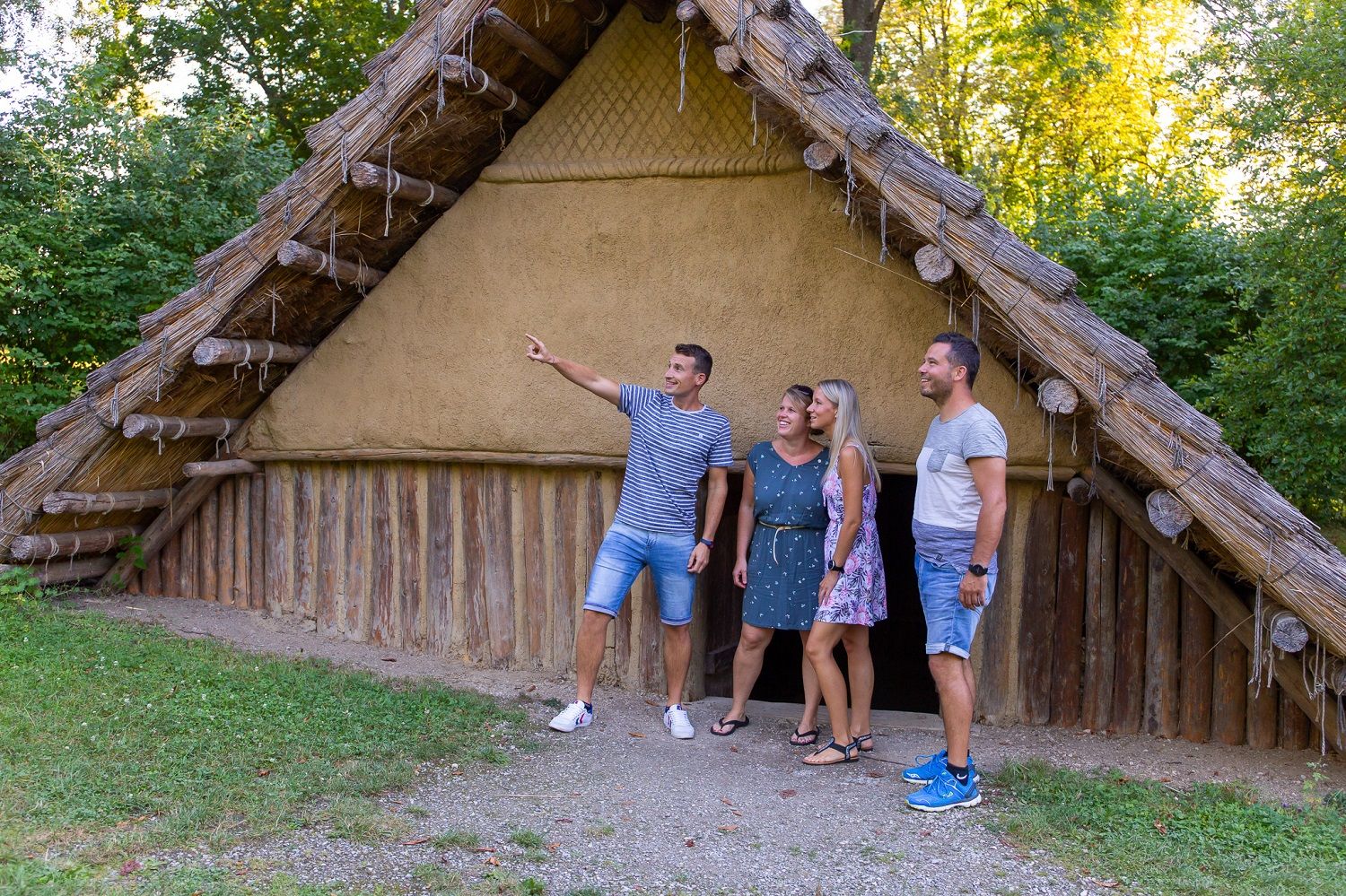 Vier Personen stehen vor einem rekonstruierten prähistorischen Haus im Freien.