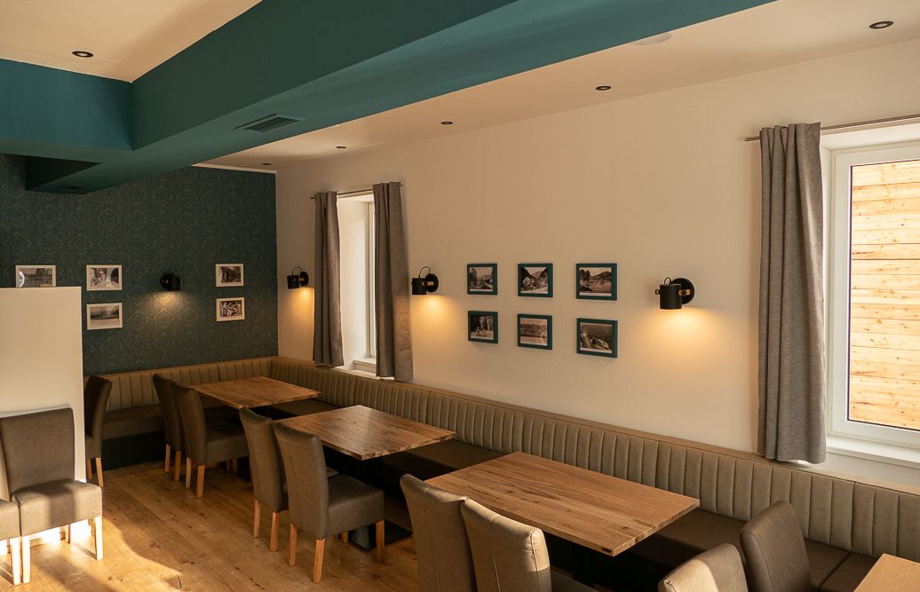 Innenansicht eines Restaurants mit Holztischen, gepolsterten Bänken und Stühlen, dekoriert mit Bildern an den Wänden.