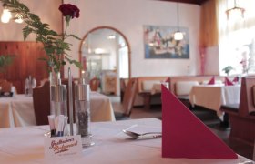 Innenansicht eines gem&uuml;tlichen Restaurants mit gedeckten Tischen, roten Servietten und einer Rose in einer Vase.