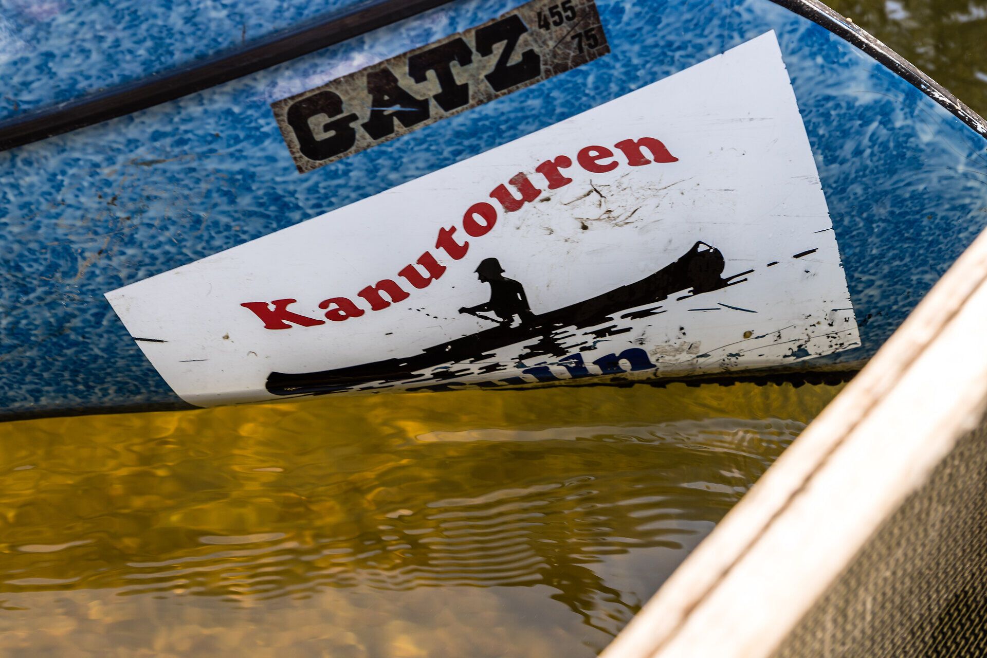 Vorderteil eines Kanus im Wasser mit einem Werbeaufdruck Kanutouren.