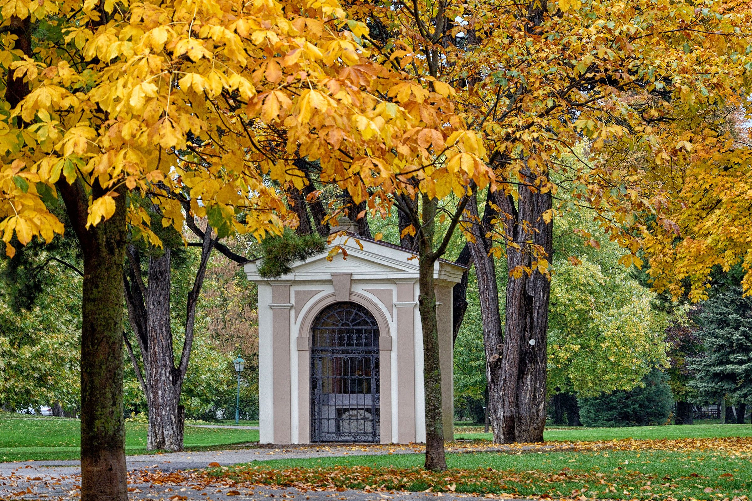 Ein kleines Gebäude in einem Park, umgeben von Bäumen mit gelbem Herbstlaub.
