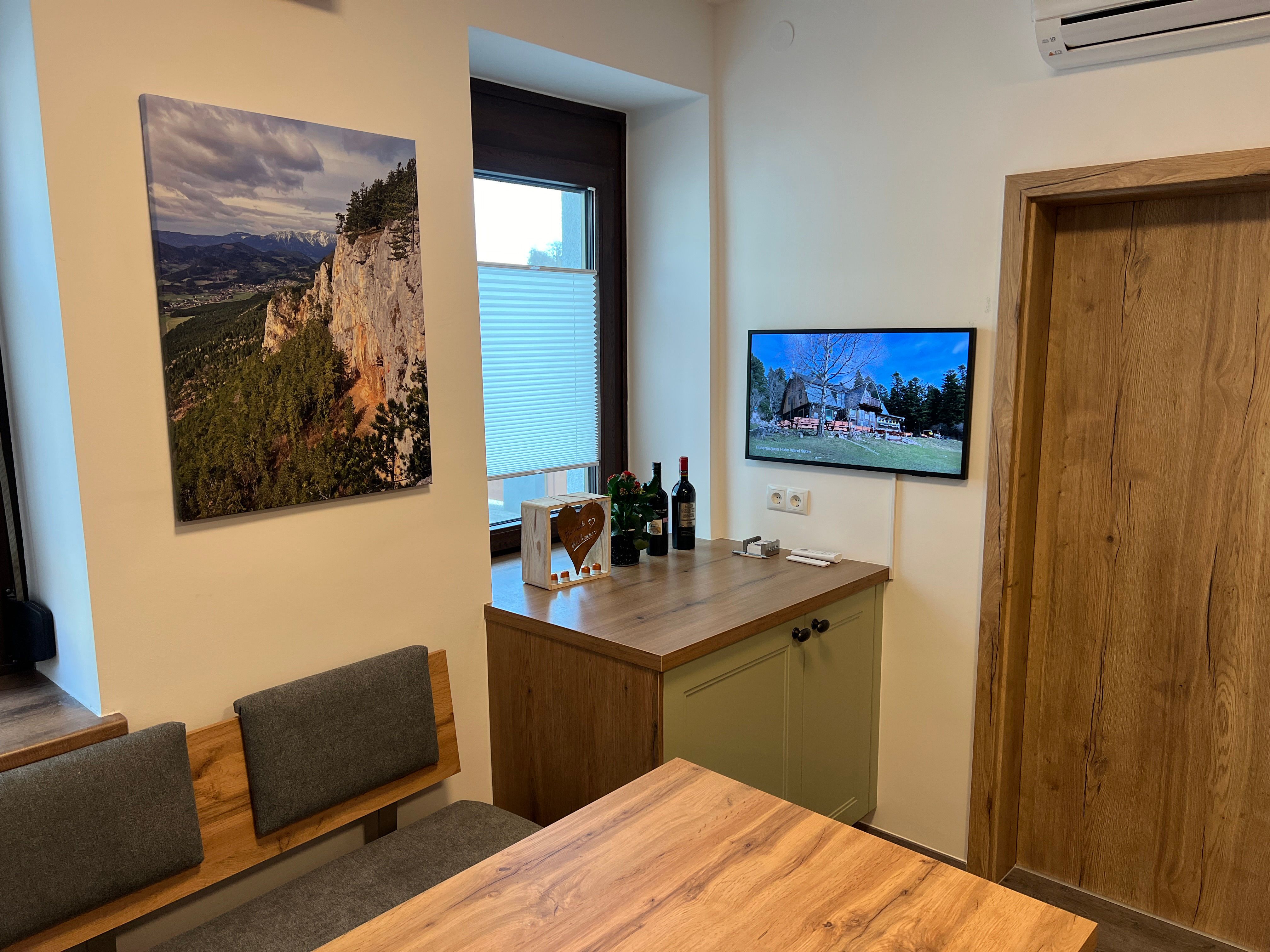 Küche mit Holzmöbeln, einem Landschaftsbild an der Wand und einem Fernseher, der ein Bild von einem Haus zeigt.