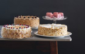 Verschiedene Torten und Geb&auml;ck auf einem Tisch vor dunklem Hintergrund.