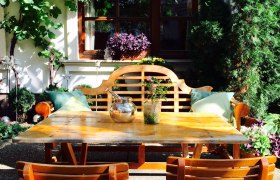 Gemütlicher Gartenbereich mit Holztisch und Stühlen, umgeben von Pflanzen und Weinreben.